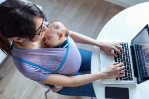 madre joven trabajando en el computador con su bebe en un fular.