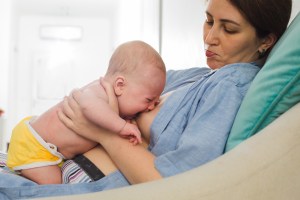 una mama intenta amamantar a su bebe reclinada hacia atras y el bebe llora