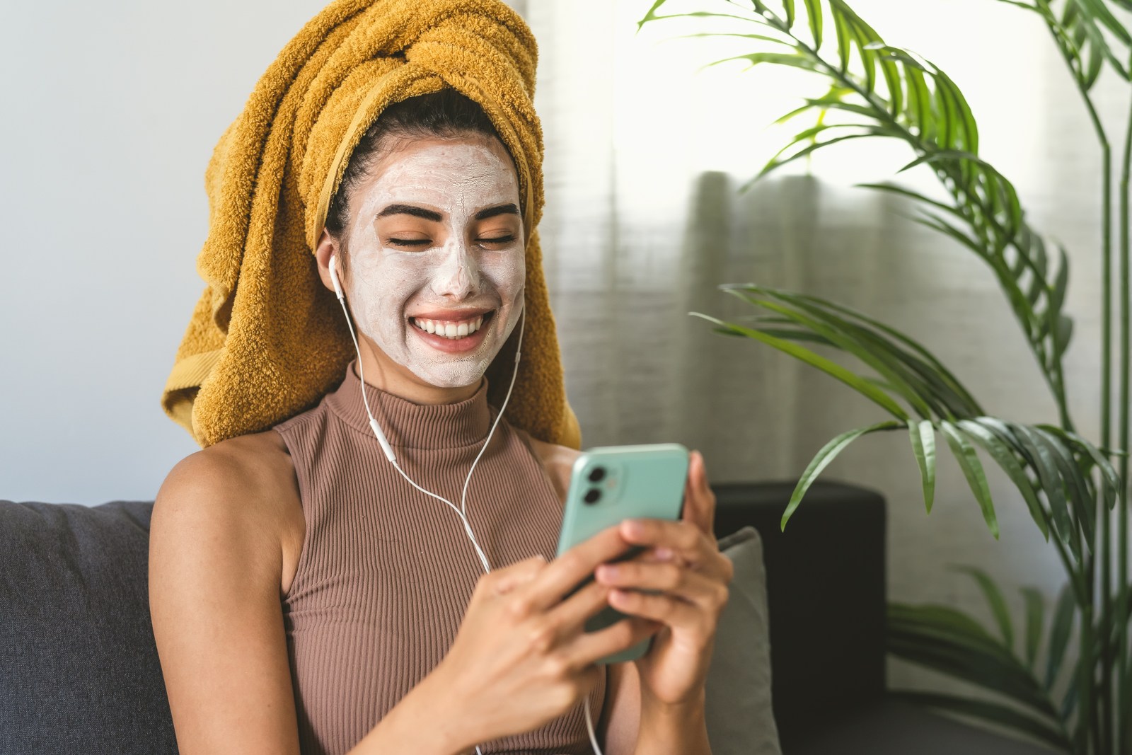 mujer mira al telefono con una toalla en la cabeza y crema facial aplicada