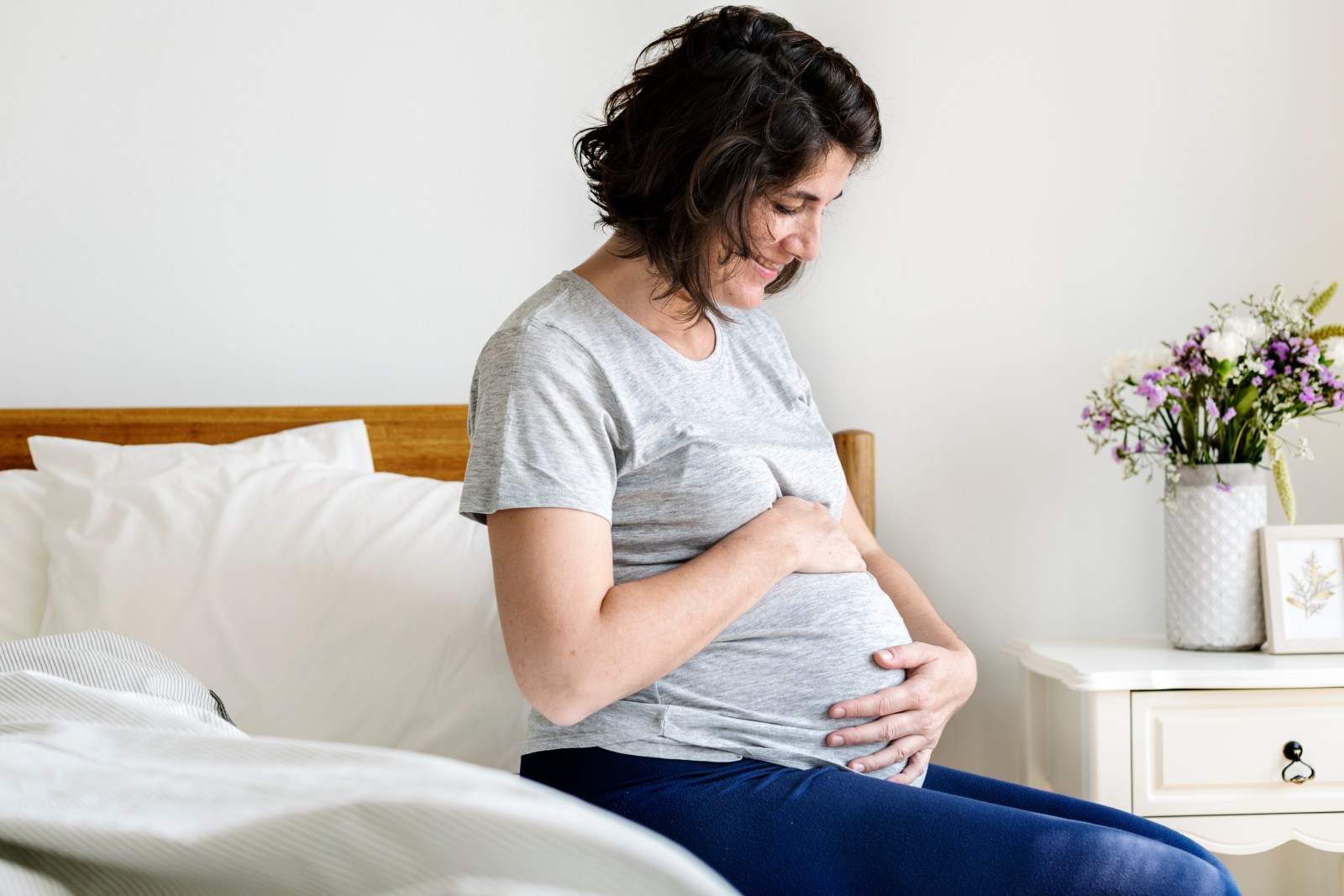 mujer embarazada sentada en su cama tocandose el vientre feliz